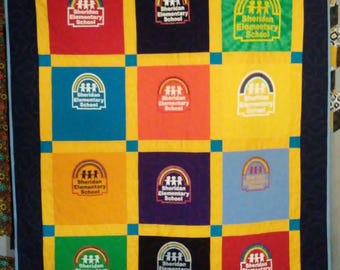 May include: A colorful quilt featuring the "Sheridan Elementary School" logo in various colors. The quilt has a dark blue border and is divided into squares of red, black, yellow, blue, orange, purple, and green, each with the school's logo.