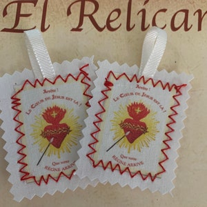 Puede incluir: Dos tarjetas de oración religiosas de tela blanca con costuras rojas alrededor de los bordes. Cada tarjeta presenta un corazón rojo con una corona de espinas y una lanza, rodeado de un sol amarillo. El texto en las tarjetas dice "Arrête! Le Coeur de Jésus est la! Que votre Règne Arrive".