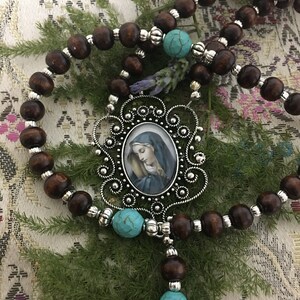 May include: A brown wooden rosary with turquoise beads and a silver pendant featuring a framed image of the Virgin Mary.