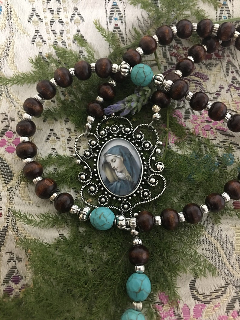 May include: A brown wooden rosary with turquoise beads and a silver pendant featuring a framed image of the Virgin Mary.