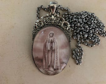 Può includere: Una collana con ciondolo in argento e un ciondolo ovale in vetro con l'immagine in bianco e nero di una donna con un lungo abito bianco. La catena è in argento e ha un design delicato.
