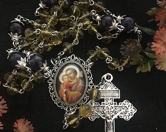 May include: A silver rosary with a crucifix and a medal of Saint Jude Thaddeus. The rosary beads are made of clear glass and amethyst. The crucifix is ornate and features a figure of Jesus Christ. The medal is round and features an image of Saint Jude Thaddeus.