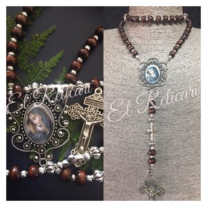 May include: A brown wooden rosary with silver beads and a silver pendant featuring a depiction of the Virgin Mary. The pendant is surrounded by a decorative silver frame. The rosary also includes a silver crucifix with a figure of Jesus Christ.