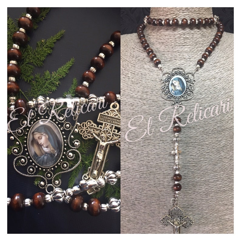 May include: A brown wooden rosary with silver beads and a silver pendant featuring a depiction of the Virgin Mary. The pendant is surrounded by a decorative silver frame. The rosary also includes a silver crucifix with a figure of Jesus Christ.