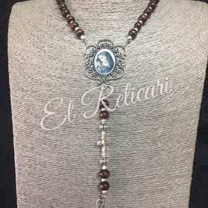 May include: A brown wooden rosary with a silver pendant featuring a depiction of the Virgin Mary. The pendant is surrounded by an ornate silver frame. The rosary also has a silver crucifix with the inscription "Ecce Homo Filius Dei Salvator" at the bottom.