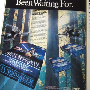 May include: A vintage advertisement for the movie "Star Wars: Return of the Jedi" on VHS. The ad features a blue and green forest background with a close-up of the VHS tape cover. The text on the ad reads "The Movie Everyone's Been Waiting For." and "Reserve Your Copy and Enter the CBS/FOX Video Return of the Jedi Sweepstakes Now!"