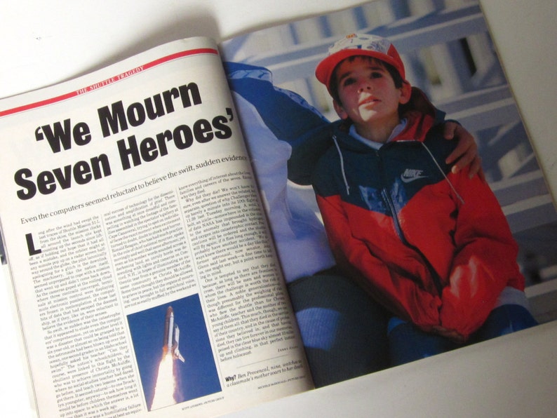 May include: A magazine cover with the headline "We Mourn Seven Heroes." The cover features a young boy wearing a red and blue jacket with the Nike logo. The boy is sitting on the lap of an adult, who is wearing a blue shirt. The magazine cover is about the space shuttle tragedy.