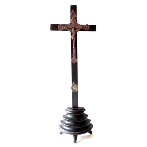May include: A black wooden crucifix with a metal Jesus figure. The crucifix is on a black wooden base with a tiered design.