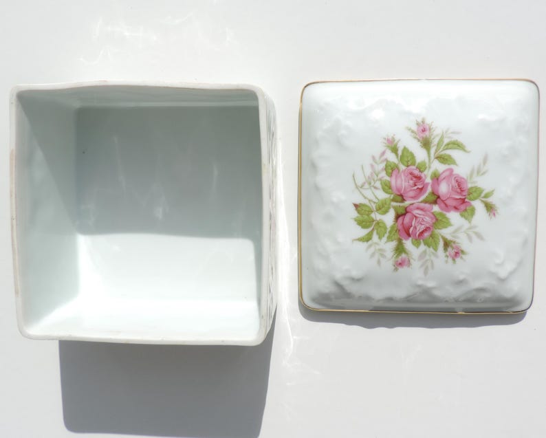 Pu&ograve; includere: Scatola quadrata in porcellana bianca con coperchio. Il coperchio presenta un motivo floreale con rose rosa e foglie verdi. La scatola &egrave; vuota.