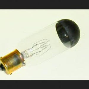 May include: A clear glass light bulb with a brass base and a black, rounded end. The internal filament is visible within the glass tube. The bulb is designed for electrical use.