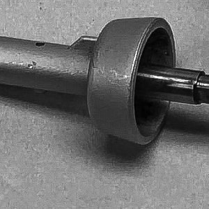 May include: A gray metal part with a round, hollowed-out section and a long, cylindrical shaft. A smaller metal shaft extends from the round section and is secured with a screw.