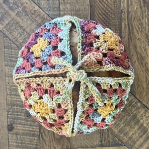 Peut inclure: Un panier à pain rond, crocheté selon un motif de granny square. Le panier présente une variété de couleurs, dont le jaune, l'orange, le vert et le violet. Une attache crochetée assortie sécurise le dessus. Le panier est conçu pour contenir une miche de pain.