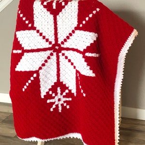 May include: A red and white crocheted throw blanket with a snowflake design. The blanket has a white crocheted border.