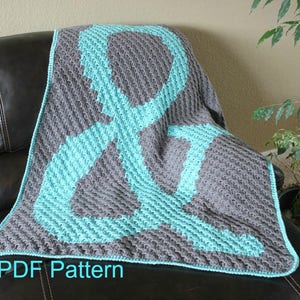 Puede incluir: Una manta de crochet con un gran diseño de ampersand en color turquesa y gris. La manta está sobre un sofá de cuero marrón. El texto "PDF Pattern" está en la parte inferior de la imagen.