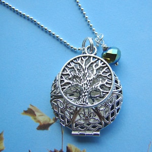 May include: A silver necklace with a tree of life pendant and a small iridescent green bead charm. The pendant is open and has a delicate filigree design.