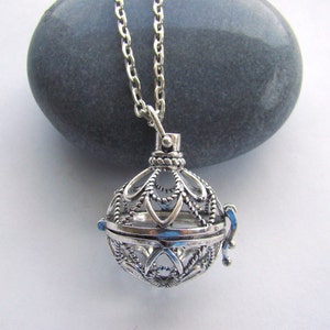 May include: A silver necklace with a delicate, ornate cage pendant. The cage is open and has a small, dangling charm.