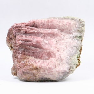Könnte beinhalten: Ein großes, raues, rosafarbenes und grünes Mineralstück mit einer geschichteten, gestreiften Textur. Das Mineral hat eine natürliche, unpolierte Oberfläche.