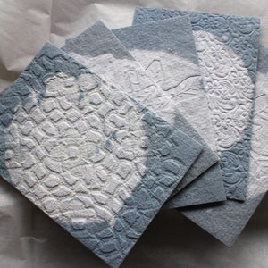 Cinco sobres de papel hechos a mano en color denim con patrones de linograbado de encaje y copos de nieve