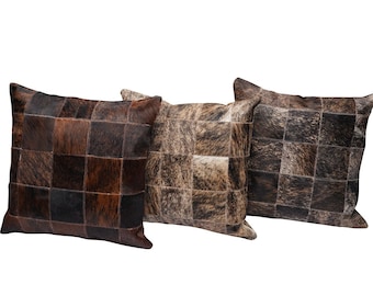 May include: Three square-shaped throw pillows with a patchwork design made of brown, black, and white cowhide.