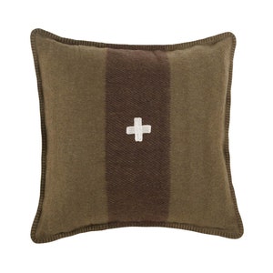 Puede incluir: Cojín decorativo cuadrado en tonos verde oliva y marrón. Presenta una franja central marrón con una cruz blanca. Los bordes están rematados con costuras marrón oscuro, creando una apariencia rústica y texturizada. Ideal para decoración.