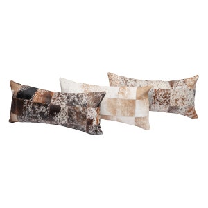 May include: Three rectangular pillows with a patchwork design made of cowhide. The pillows are in shades of brown, black, and white.