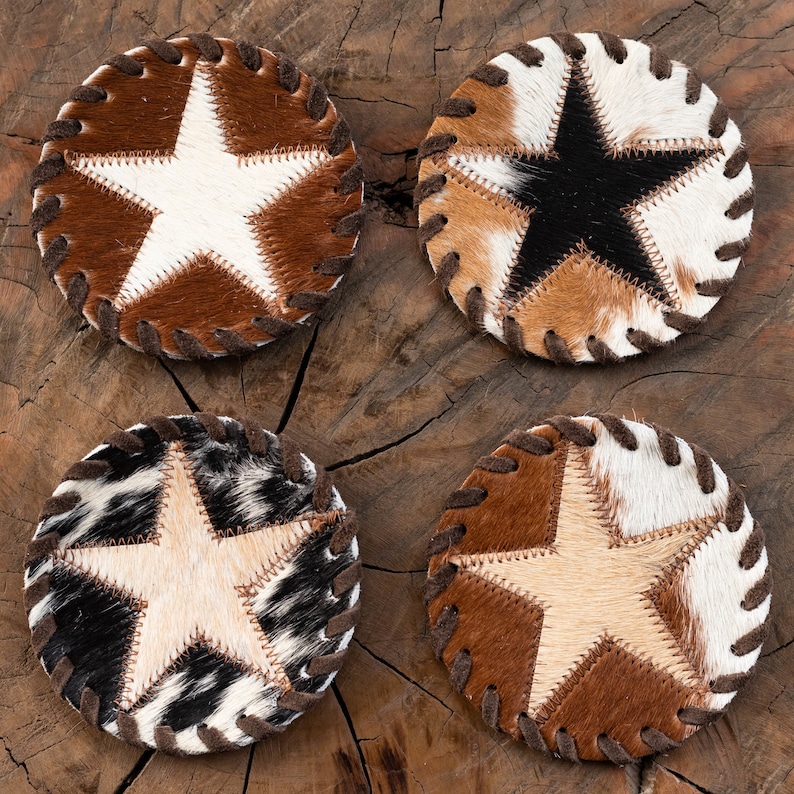 May include: Four round cowhide coasters with a star design. Each coaster features a different color star: white, black, brown, and cream. The coasters are stitched together with brown thread.