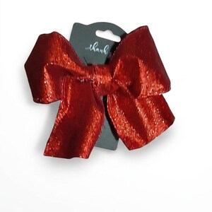 May include: A large, vibrant red hair bow with a shimmering, glittery texture. The bow is attached to a dark grey display card that features the text thank you printed in a white, cursive script at the top centre of the card.