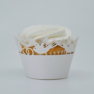 May include: White cupcake with white frosting and a white lace paper wrapper with a bird and ring design.