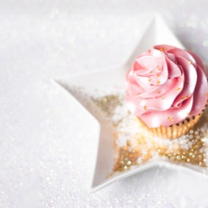May include: A pink cupcake with gold sprinkles on top, sitting on a white star-shaped plate with gold glitter.