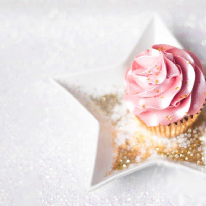 May include: A pink cupcake with gold sprinkles on top, sitting on a white star-shaped plate with gold glitter.
