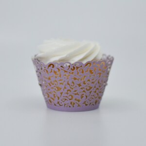 May include: A lavender cupcake wrapper with a delicate lace design. The wrapper is made of paper and has a scalloped edge. The cupcake is topped with white frosting.