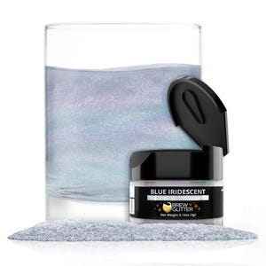 May include: A clear glass filled with a light blue liquid, next to a small jar of blue iridescent edible glitter. The jar has a black lid and a label that reads "BLUE IRIDESCENT" and "BREW GLITTER". A small pile of glitter is in front.