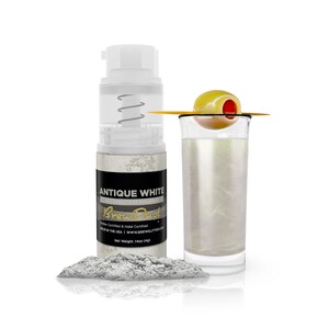 May include: A bottle of Antique White Brew Dust edible glitter, a white powder with a pearlescent sheen. The bottle is labeled with the product name and the company's website. The glitter is shown in a glass with a green olive.
