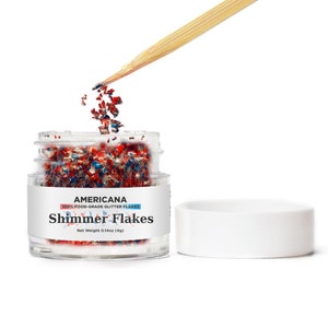 May include: A small clear jar filled with red, white, and blue glitter flakes. The jar has a white label that reads "Americana 100% Food-Grade Glitter Flakes Shimmer Flakes Net Weight 0.14oz (4g)".