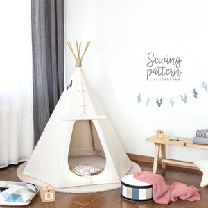 Könnte beinhalten: Ein weißes Tipi-Zelt mit einem Holzgestell und einer braunen Stoffbasis. Das Tipi ist in einem Raum mit einer weißen Wand und einer Holzbank aufgebaut. Die Wand hat ein Banner mit dem Text "Sewing pattern LARGE TEEPEE".