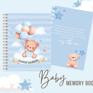 May include: A blue and white baby memory book with a cute teddy bear holding balloons. The cover has the text "Alexis Gabriel" and "My little one." The book is titled "Baby Memory Book".
