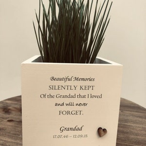 Op de afbeelding: Een vierkante, crèmekleurige plantenbak met de tekst "Beautiful Memories SILENTLY KEPT Of the Grandad that I loved and will never FORGET." en de naam "Grandad" met data. Bevat groen gras.
