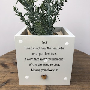 Puede incluir: Una maceta cuadrada de color gris claro con una planta verde. La maceta tiene la palabra "Dad" y un mensaje: "El tiempo no puede curar el dolor ni detener una lágrima silenciosa. No se llevará los recuerdos de alguien a quien amábamos tanto. Te echamos de menos siempre x."