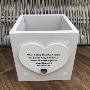 Puede incluir: Una maceta de madera blanca con un adorno en forma de corazón. El corazón tiene el texto "When it comes to Aunties & Uncles and the nice things that they do there's not a couple anywhere as special as you t. Love Jake & Olly x."