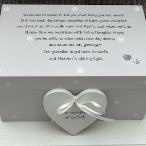 Puede incluir: Una caja de recuerdos de madera gris con un adorno en forma de corazón blanco atado con una cinta blanca. La caja tiene lunares y texto: "No hay palabras para decir lo que significó perderte..." El corazón dice "Mis recuerdos de mi papá."