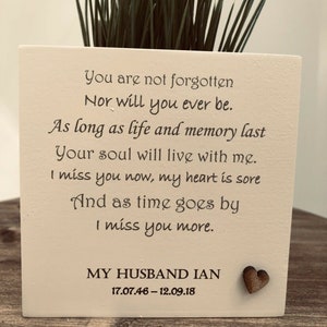 May include: A square, off-white planter with a heartfelt message and a small wooden heart. The text reads, "You are not forgotten...I miss you more." The planter contains green grass. The bottom of the planter reads "MY HUSBAND IAN 17.07.46-12.09.18."