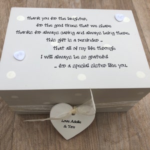 May include: A cream-coloured wooden gift box with a heart-shaped tag. The box is decorated with a polka dot pattern and a ribbon. The text on the box reads: "thank you for the laughter...for a special sister like you." The tag says "Love Adelle & Tam."