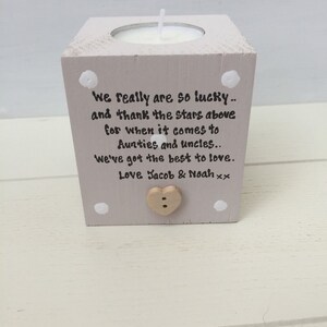 Puede incluir: Un portavelas cuadrado de madera gris claro con una vela blanca. La parte frontal del soporte tiene el texto "We really are so lucky.. and thank the stars above for when it comes to Aunties and uncles.. We've got the best to love. Love Jacob & Noah xx."