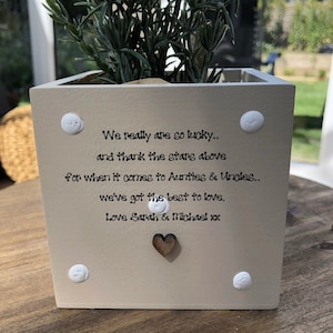 Puede incluir: Una maceta cuadrada de color crema con una planta. La maceta tiene el texto "We really are so lucky.. and thank the stars above for when it comes to Aunties & Uncles.. we've got the best to love. Love Sarah & Michael xx."