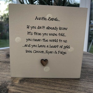 Puede incluir: Una maceta cuadrada blanca con el texto "Auntie Sarah.. If you don't already know it's time you were told.. you mean the world to us..and you have a heart of gold. Love Connor, Ryan & Paige." Un pequeño corazón de madera está adherido al frente.