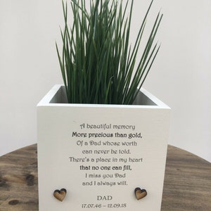 Puede incluir: Jardinera de madera blanca con hierba verde, con un mensaje conmemorativo y adornos de corazón de madera. El texto dice: "Un hermoso recuerdo... Te echo de menos papá y siempre lo haré. PAPÁ 17.07.46 - 12.09.18."