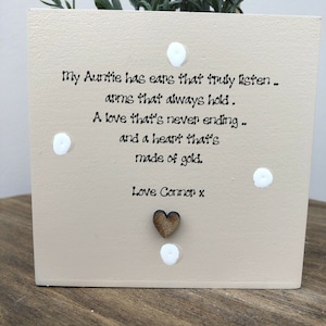 Puede incluir: Un bloque de madera cuadrado beige con el texto "My Auntie has ears that truly listen... arms that always hold. A love that's never ending... and a heart that's made of gold. Love Connor x." Puntos blancos decorativos y un corazón de madera adornan el bloque.