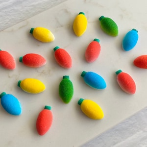 Puede incluir: Surtido de caramelos de colores en forma de bombilla con tapas verdes. Los caramelos están dispuestos sobre una superficie de mármol blanco.