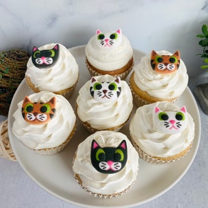 Puede incluir: Seis cupcakes decorados con glaseado blanco y caras de gato de fondant. Los gatos tienen diferentes colores de pelaje, incluyendo negro, blanco, naranja y atigrado.