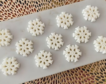 May include: Twelve white snowflake-shaped decorations on a white marble surface. The snowflakes are arranged in a circular pattern.